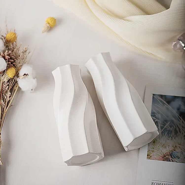Pair of modern white ceramic vases on a table with dried flowers and soft fabric