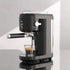 Modern black espresso machine making coffee in a clear glass on a reflective countertop