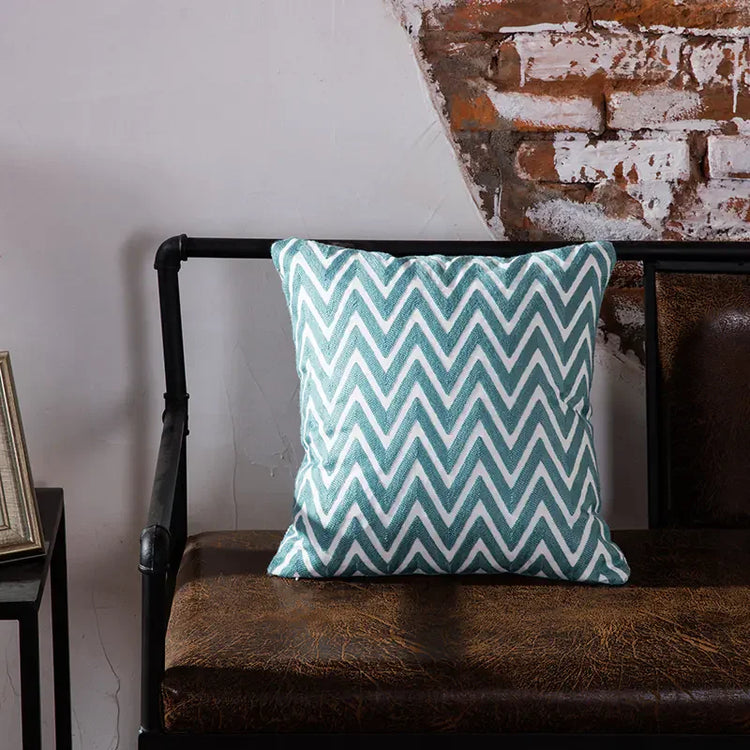 Blue and white chevron throw pillow on rustic leather bench against exposed brick wall
