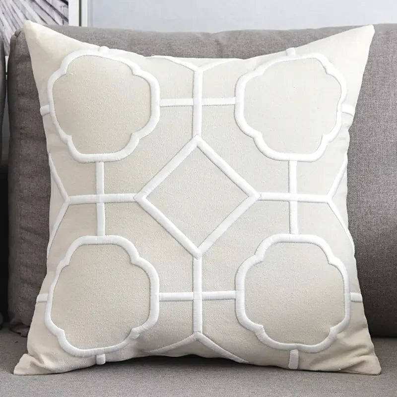 Beige decorative throw pillow with geometric white embroidery on grey sofa