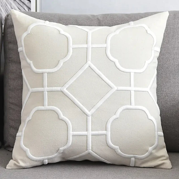 Beige decorative throw pillow with geometric white embroidery on grey sofa