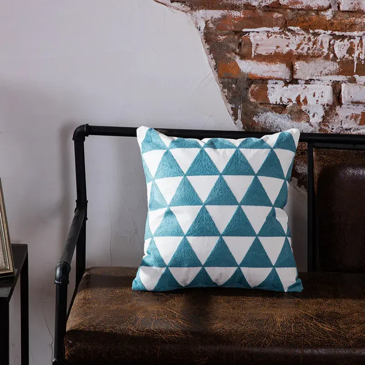 Blue and white geometric pillow on brown leather bench with exposed brick wall