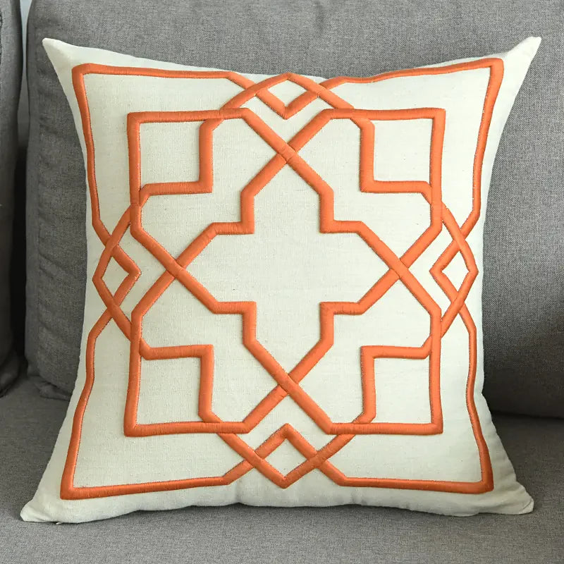 Modern beige throw pillow with orange geometric embroidery on a gray sofa