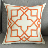 Modern beige throw pillow with orange geometric embroidery on a gray sofa