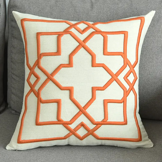 Modern beige throw pillow with orange geometric embroidery on a gray sofa