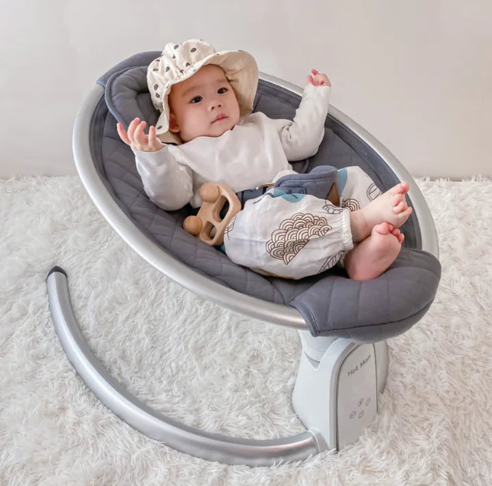 Baby in polka dot hat sitting in modern gray baby rocker on white fluffy rug