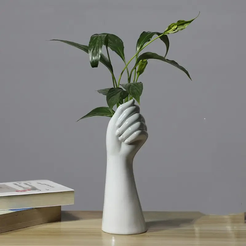 White ceramic hand vase holding green plant on wooden desk with books
