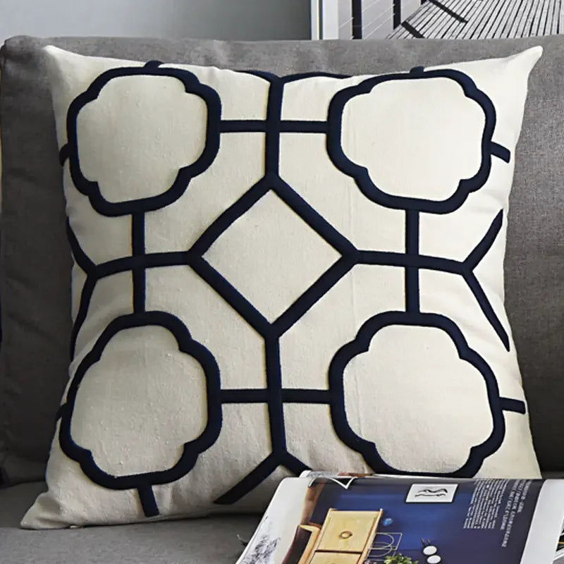 Cream decorative pillow with geometric black pattern on a gray sofa