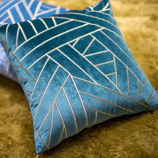 Blue velvet throw pillow with gold geometric pattern on a shaggy rug