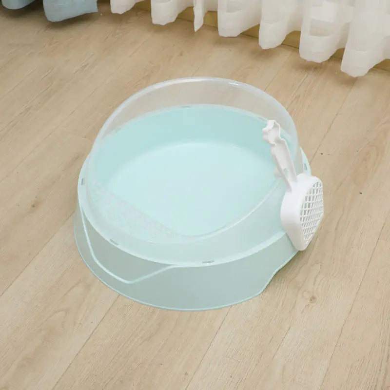Light blue cat litter box with sifting scoop on wooden floor near white curtains