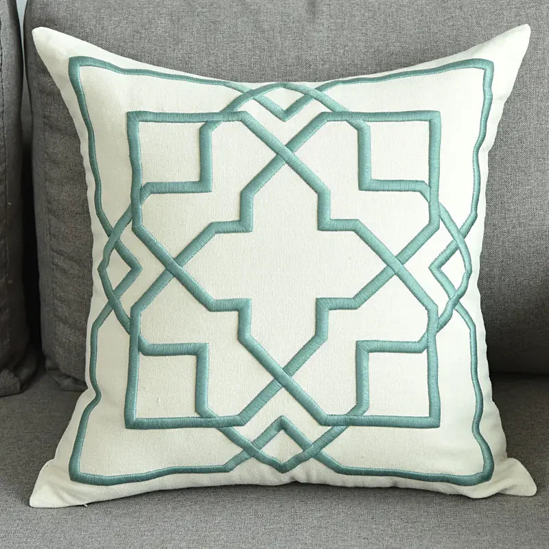 Modern decorative pillow with geometric teal embroidery on a gray sofa
