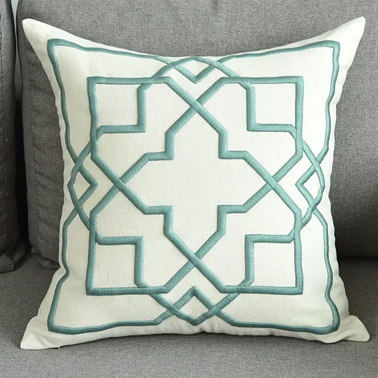Modern decorative pillow with geometric teal embroidery on a gray sofa