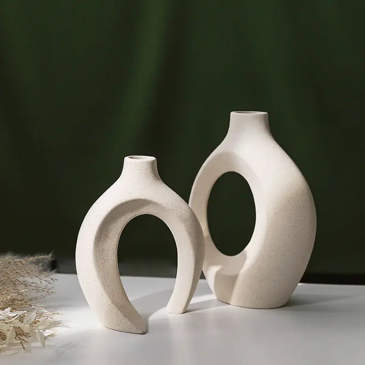Modern ceramic vases with abstract, sculptural hollow design on white table