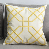 Cream decorative throw pillow with yellow geometric embroidery on a grey sofa