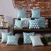 Assorted teal and white geometric throw pillows on a bench against a rustic brick wall