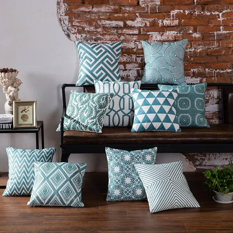 Assorted teal and white geometric throw pillows on a bench against a rustic brick wall
