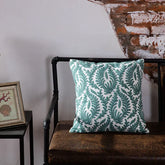 Decorative green leaf pattern pillow on brown bench against rustic brick wall