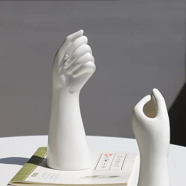 Modern white ceramic hand sculptures on a table with a book, minimalist home decor