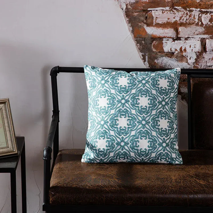 Teal patterned throw pillow on brown leather bench against exposed brick wall decor