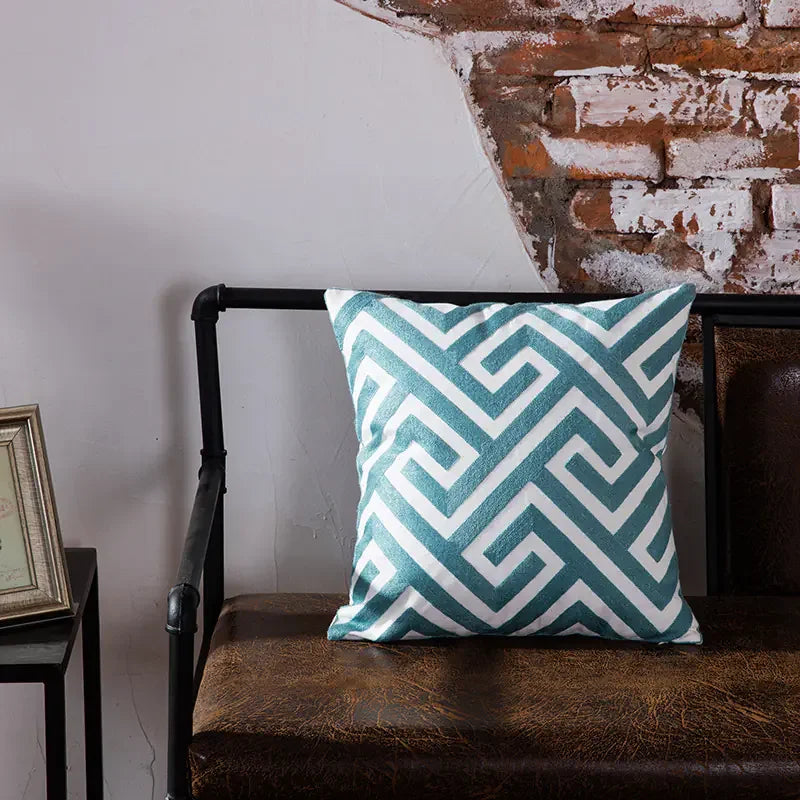 Geometric blue and white throw pillow on brown leather bench against exposed brick wall