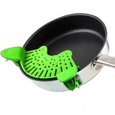 Green silicone pot strainer clipped onto a stainless steel frying pan