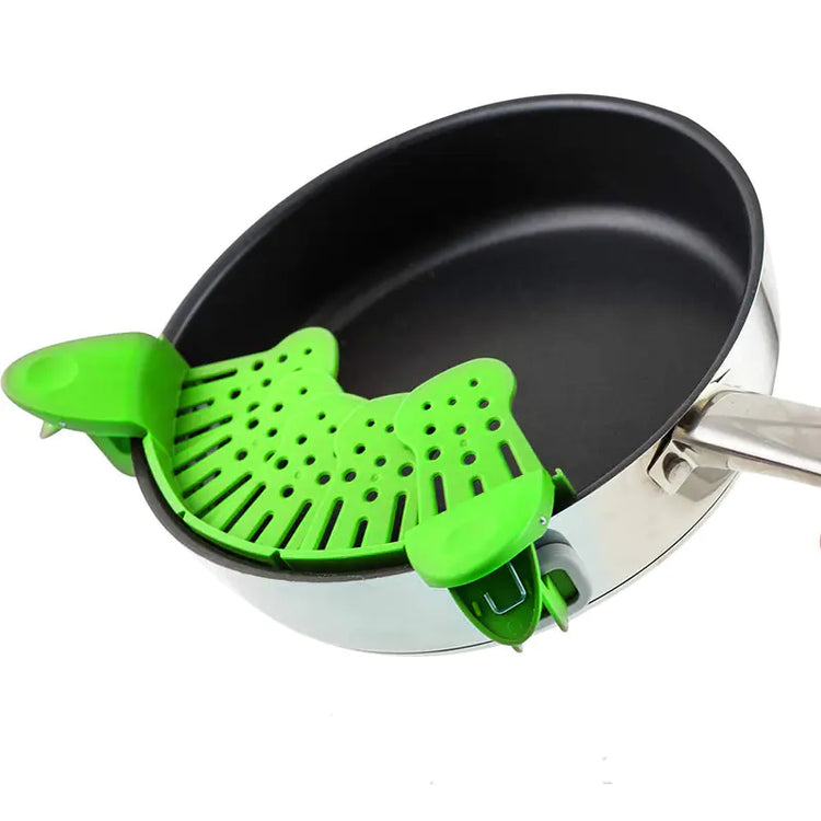 Green silicone pot strainer clipped onto a stainless steel frying pan