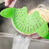 Green silicone pot strainer draining pasta water in a kitchen sink